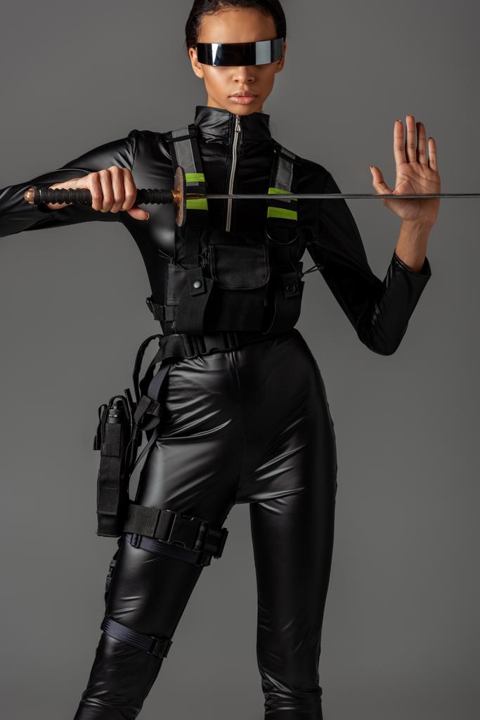 attractive futuristic african american woman in glasses with sword isolated on grey - Photo, Image