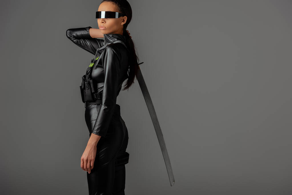 side view of futuristic African american woman in glasses with sword on grey
 - Фото, изображение