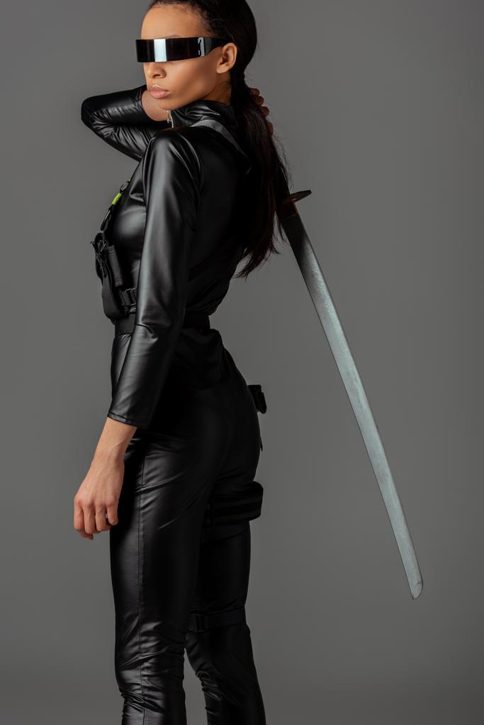side view of futuristic african american woman in glasses with sword isolated on grey - Photo, Image