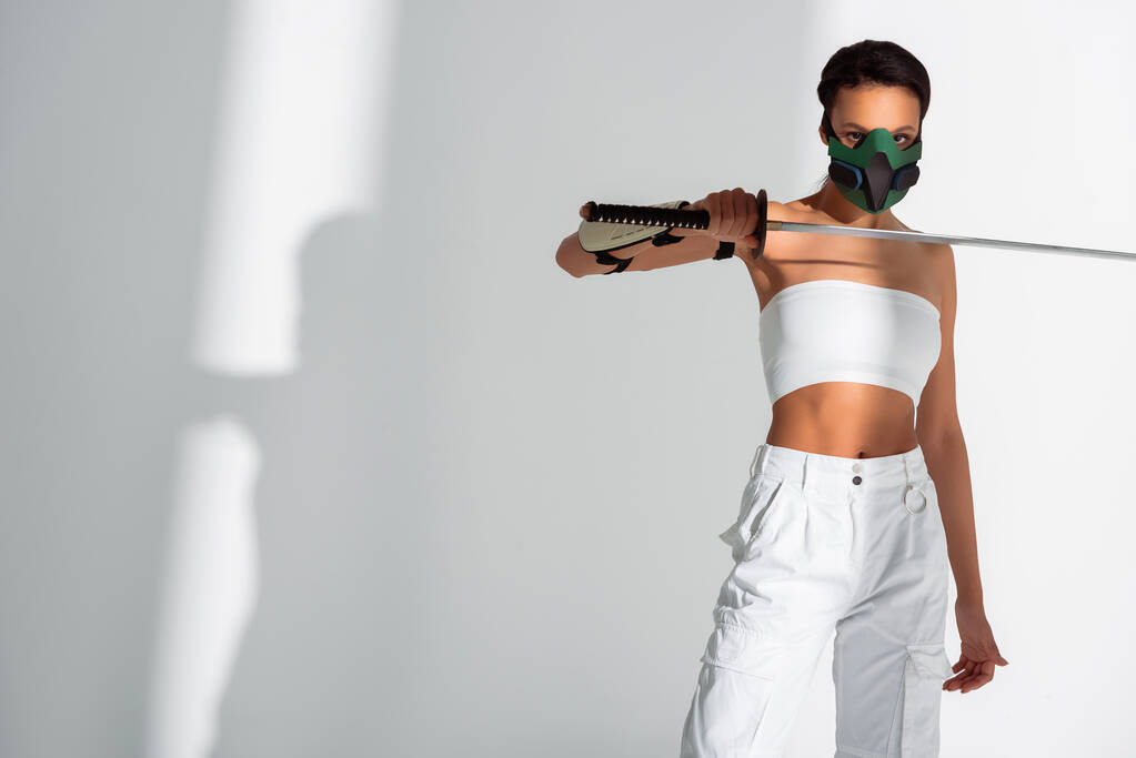 φουτουριστική Αφροαμερικανή γυναίκα με μάσκα ασφαλείας με σπαθί σε λευκό φόντο - Φωτογραφία, εικόνα