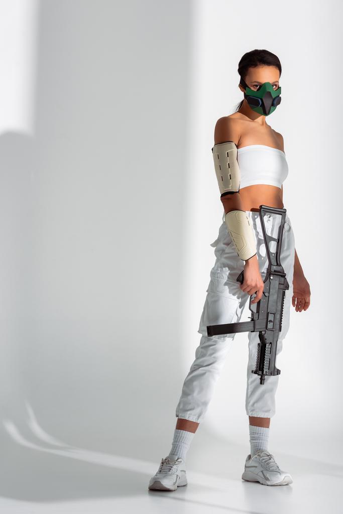 futuristic african american woman in safety mask with assault rifle on white background - Photo, Image