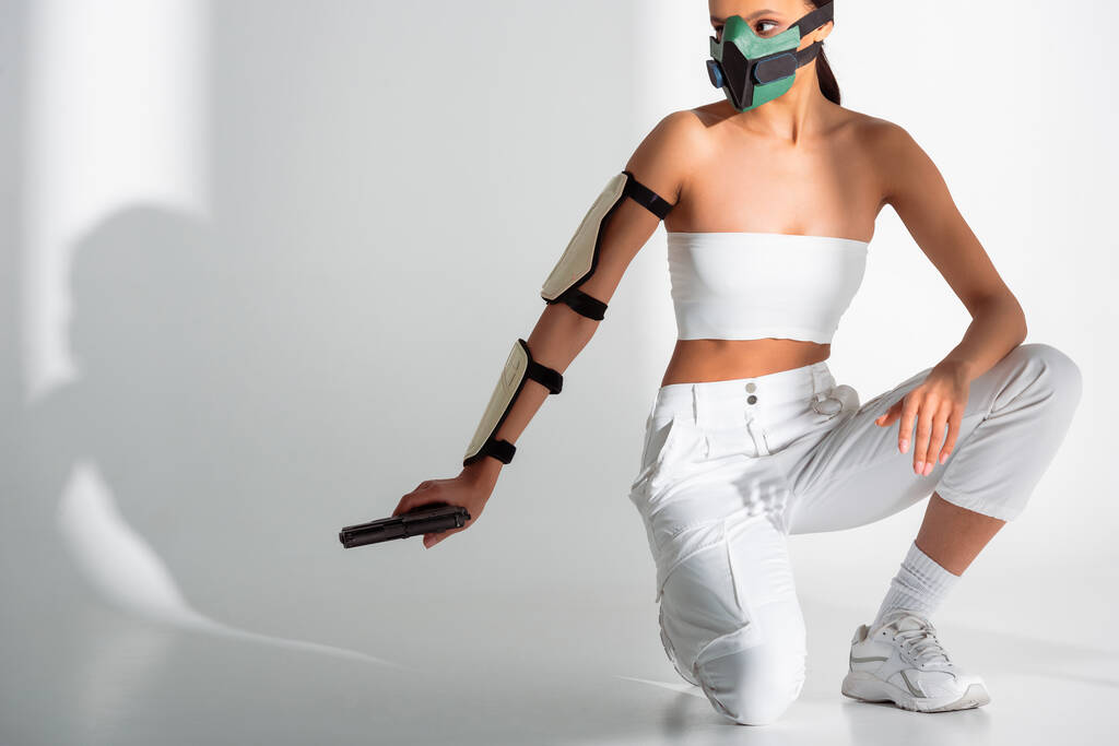 futurista Africano americano mulher em máscara de segurança com arma no fundo branco
 - Foto, Imagem