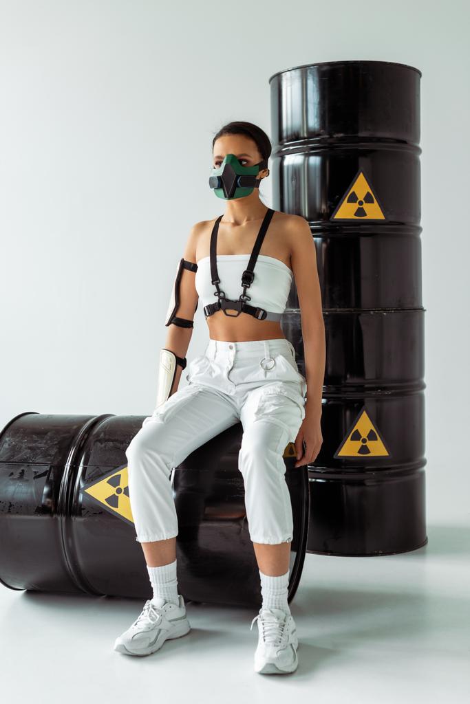 futuristische afrikanisch-amerikanische Frau in Schutzmaske und Atommüllfässern auf weißem Hintergrund - Foto, Bild