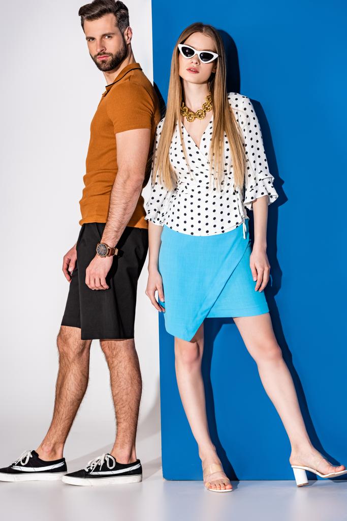 μοντέρνο νεαρό ζευγάρι ποζάρουν σε καλοκαιρινά ρούχα και γυαλιά ηλίου σε γκρι και μπλε - Φωτογραφία, εικόνα