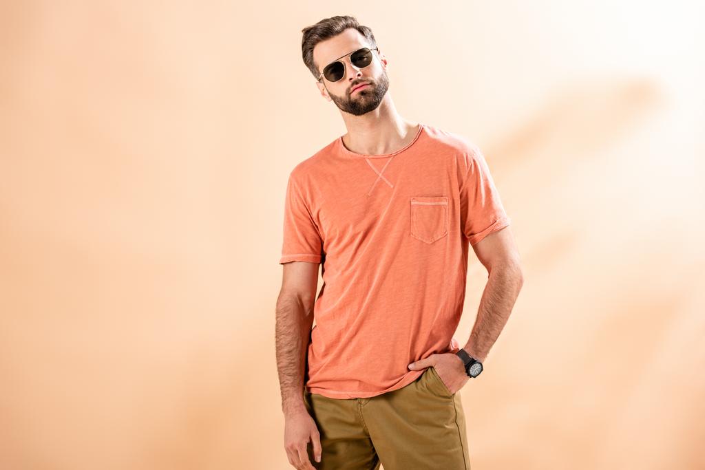 divatos fiatalember pózol rövidnadrágban, nyári pólóban és napszemüvegben bézsen - Fotó, kép