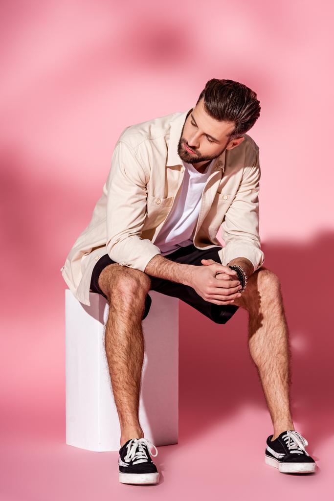 élégant homme barbu posant en chemise d'été et short sur cube blanc sur rose
 - Photo, image