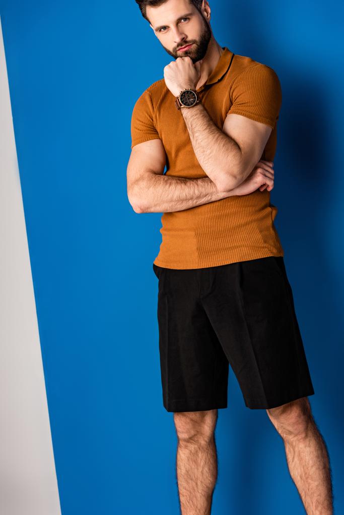 stílusos töprengő fiatalember pózol rövidnadrágban és barna póló szürke és kék  - Fotó, kép