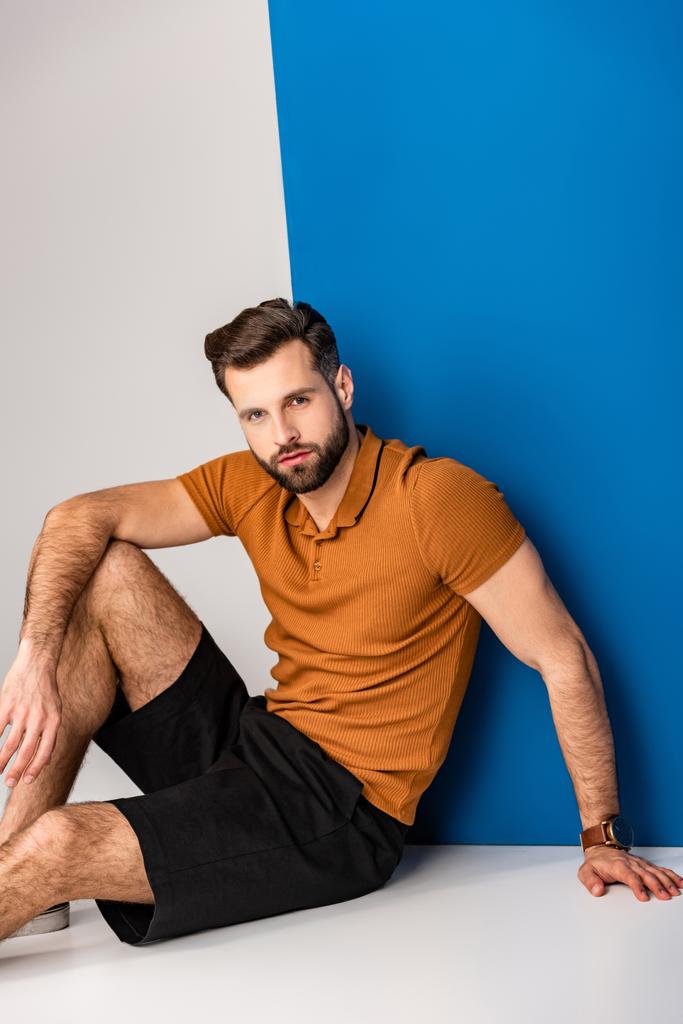 модний молодий чоловік позує в шортах і коричневому поло на сірому і синьому
  - Фото, зображення