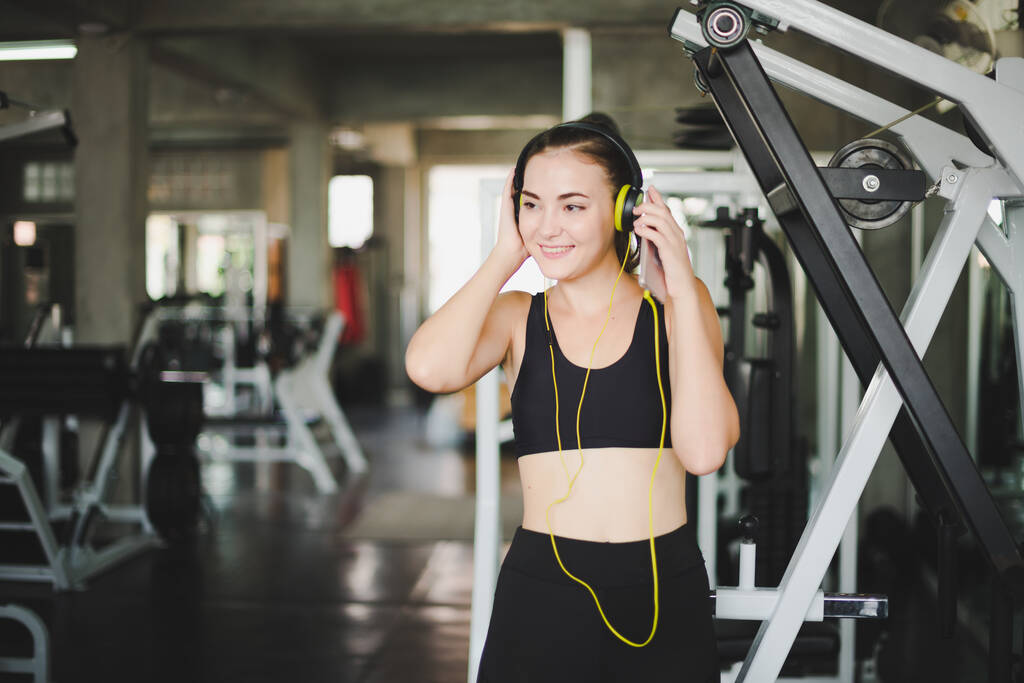 Schöne Frauen kommen ins Fitnessstudio und entspannen sich, indem sie Musik aus Kopfhörern hören. Sie trägt Sportkleidung. - Foto, Bild