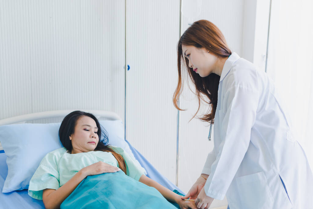 Mujer asiática médico visita a la paciente acostada en la cama del hospital
. - Foto, imagen
