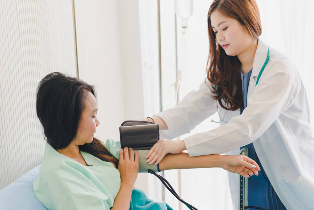 Las mujeres asiáticas los médicos vienen a medir la presión del paciente. Acostado en la cama del paciente
. - Foto, imagen