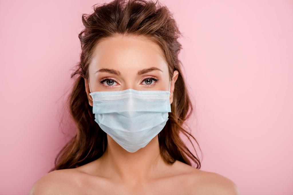mujer joven en máscara médica mirando a la cámara aislada en rosa
 - Foto, Imagen