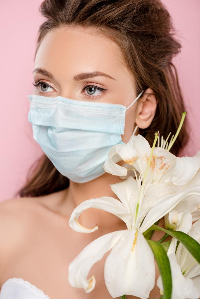 fiatal nő orvosi maszk gazdaság virágok elszigetelt rózsaszín - Fotó, kép