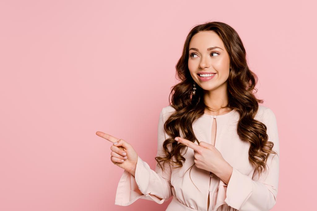 happy young woman looking away and pointing with fingers isolated on pink  - Photo, Image