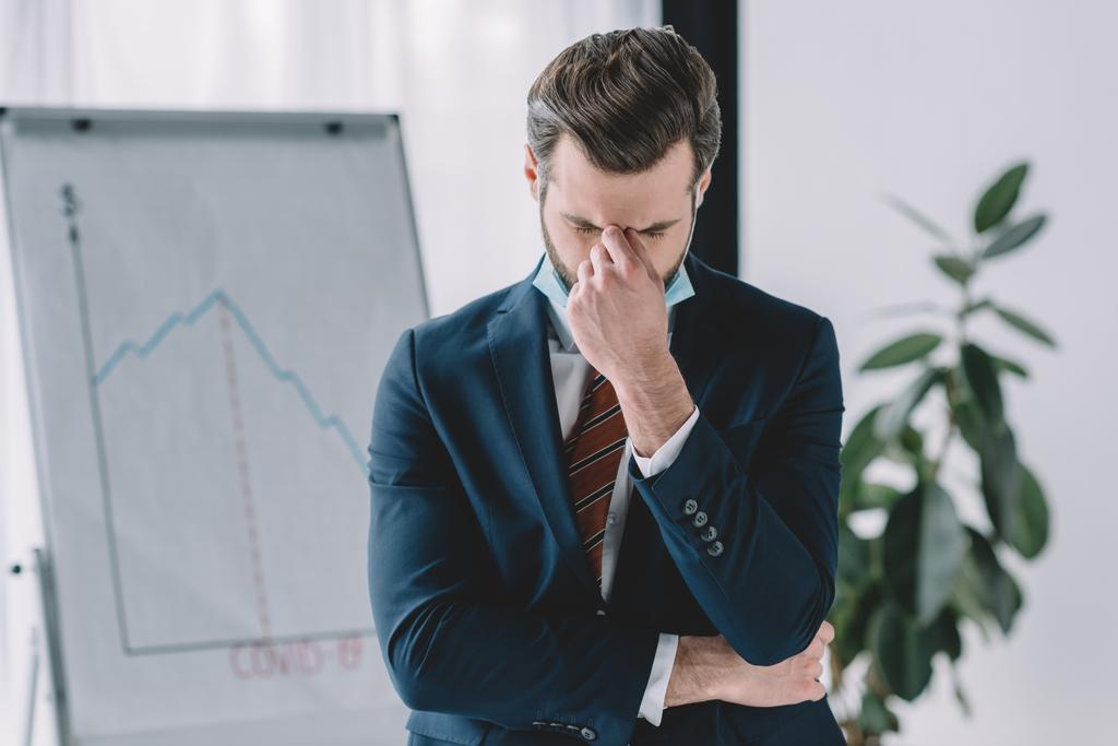 depressed businessman standing with bowed head and closed eyes near flipchart with graphs showing recession - Photo, Image