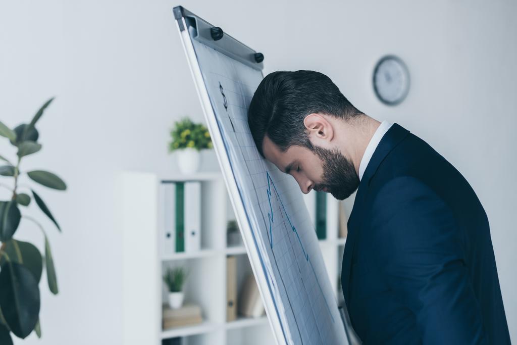 depressed businessman standing with closed eyes and leaning at flipchart with forehead  - Photo, Image
