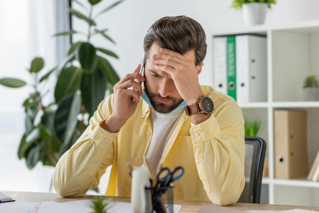 selective focus of depressed businessman touching forehead while talking on smartphone in office - Photo, Image
