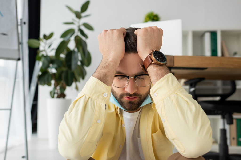 depressief zakenman houdt handen op het hoofd tijdens het zitten in het kantoor met gesloten ogen - Foto, afbeelding