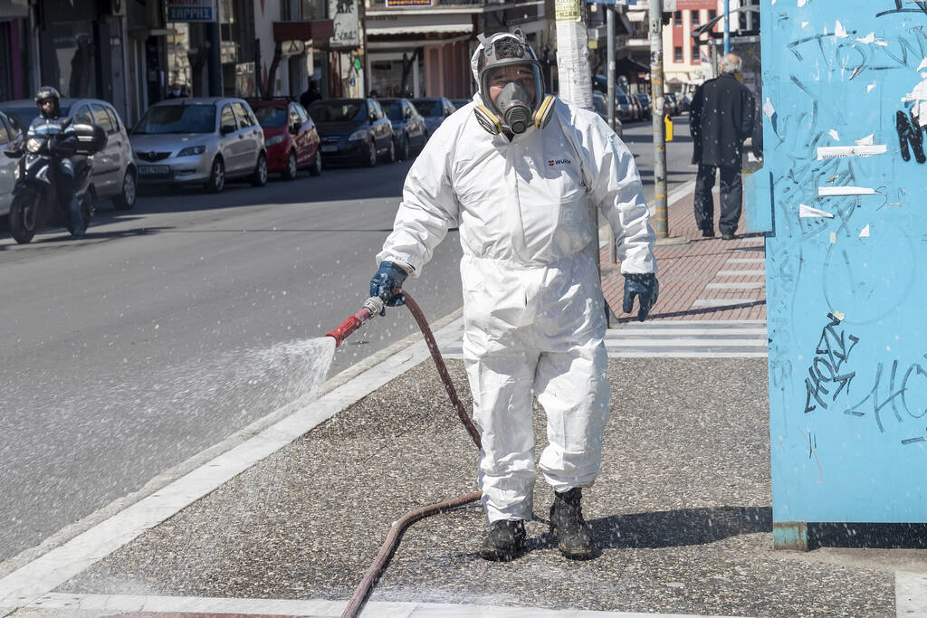 Thessalonique, Grèce - 8 avril 2020 : Des travailleurs pulvérisent du désinfectant dans le cadre de mesures préventives contre la propagation du nouveau coronavirus COVID-19 dans les rues et les places
 - Photo, image