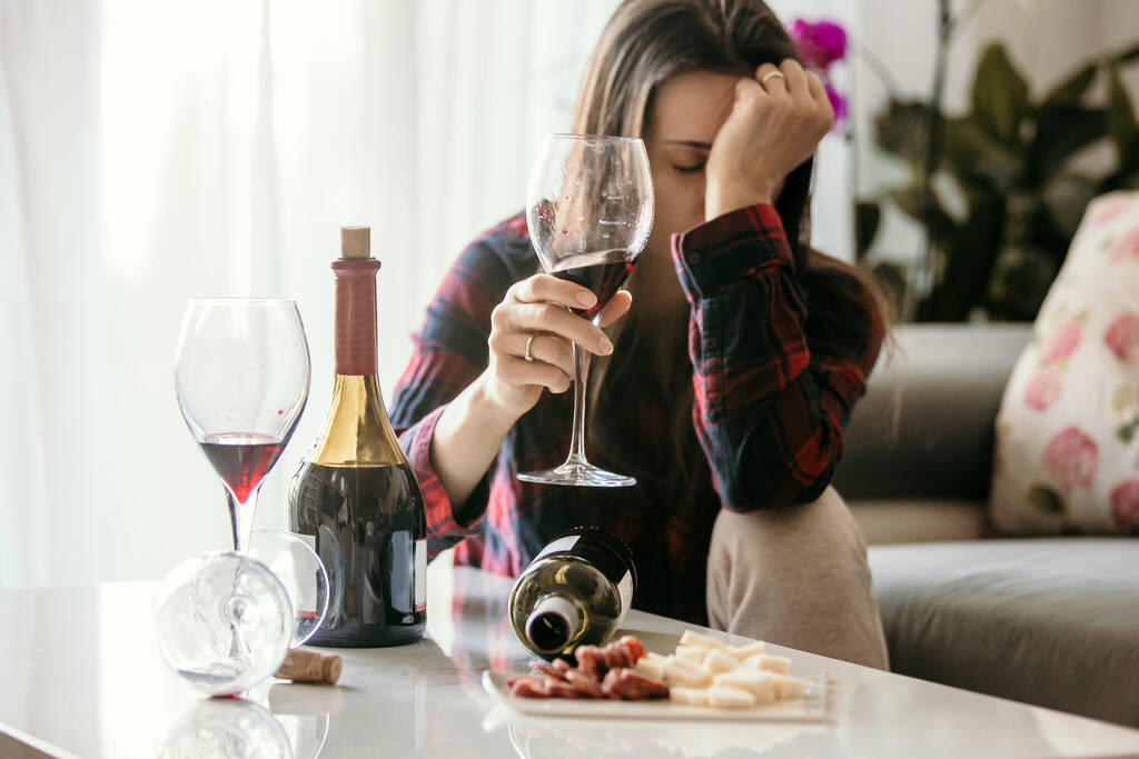 Грустная уставшая женщина, пьет вино дома, одна, сидит на полу в гостиной, чувствуя депрессию - Фото, изображение