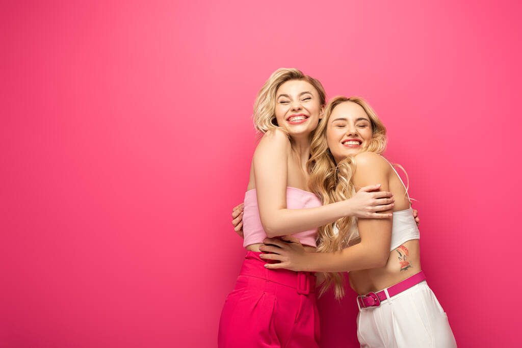 Usmívající se blondýny přátelé objímající na růžovém pozadí - Fotografie, Obrázek