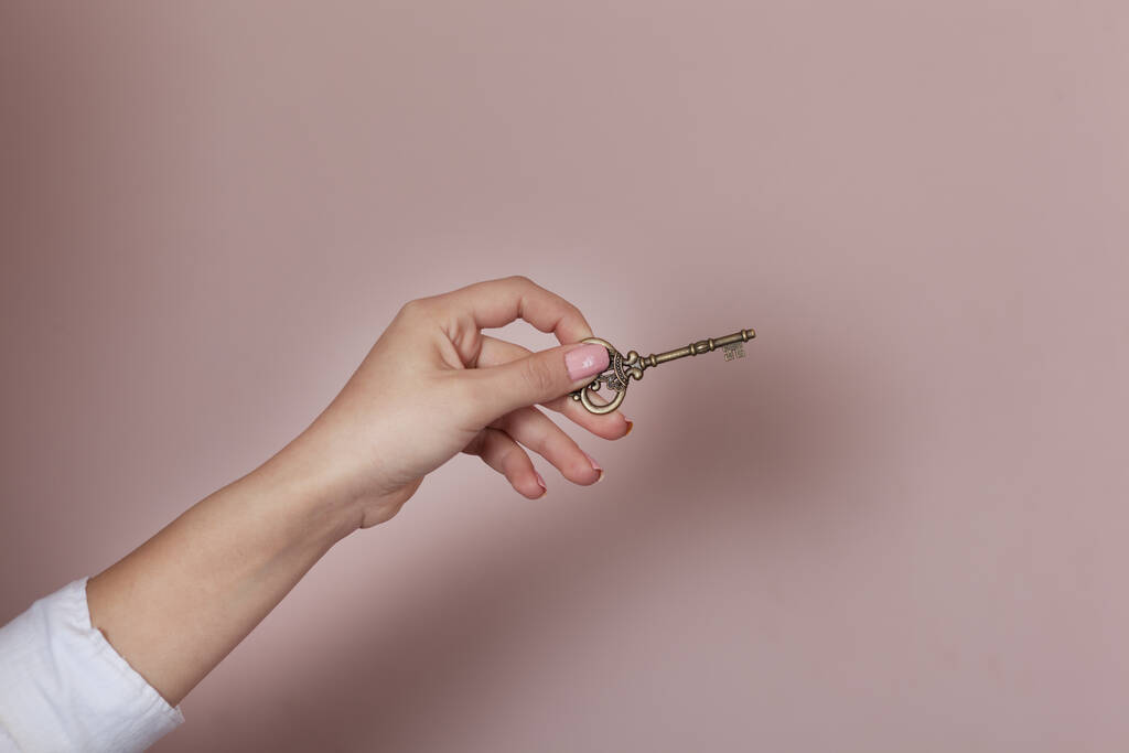 женщина держит винтажный ключ на розовом фоне
 - Фото, изображение