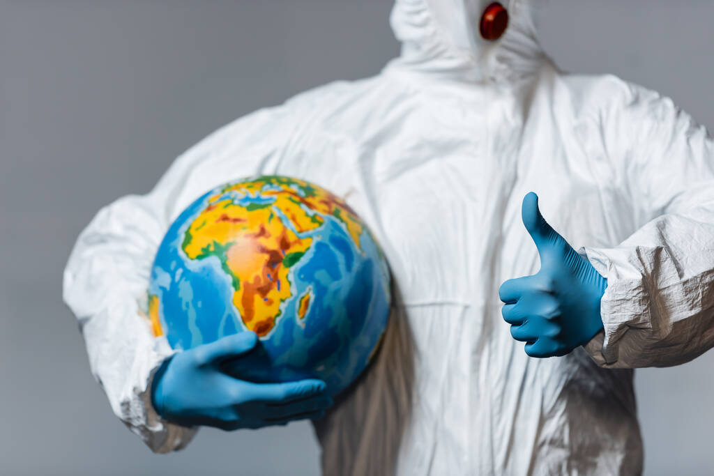 vista recortada del hombre en traje de materiales peligrosos sosteniendo globo y mostrando el pulgar hacia arriba aislado en gris
  - Foto, Imagen