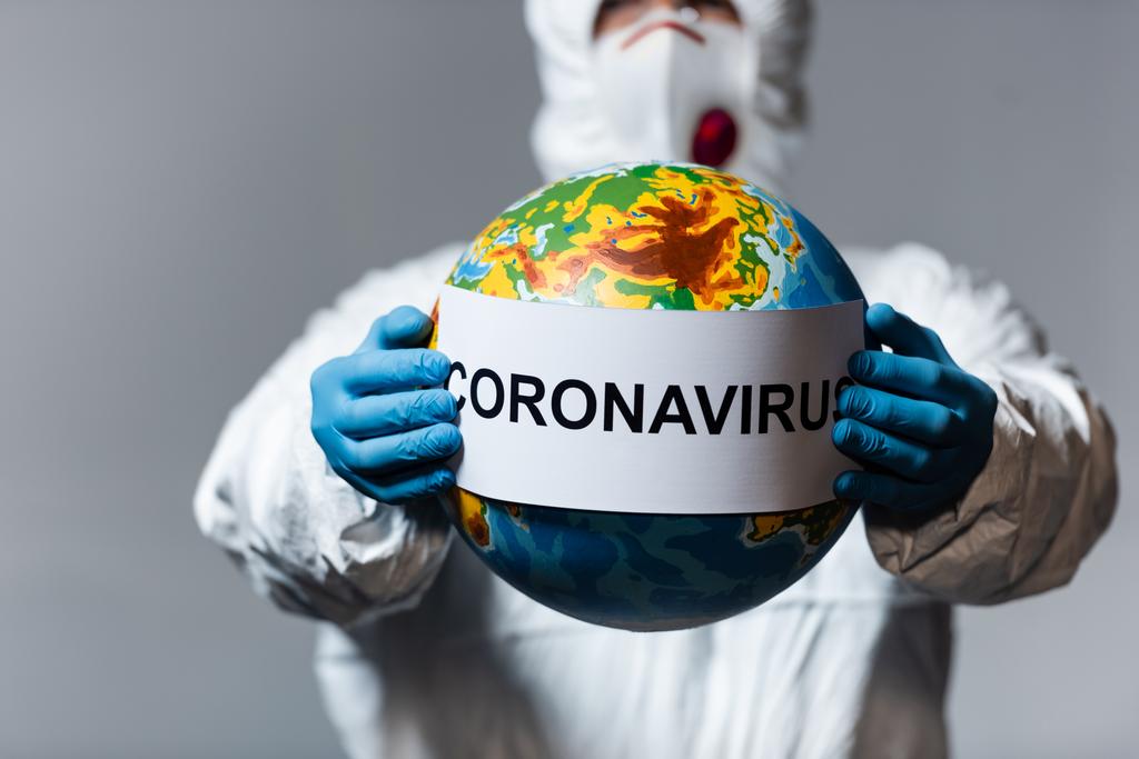 selektiivinen painopiste mies hazmat puku ja lääketieteellinen naamio tilalla maapallo ja paperi coronavirus kirjoitus eristetty harmaa
  - Valokuva, kuva