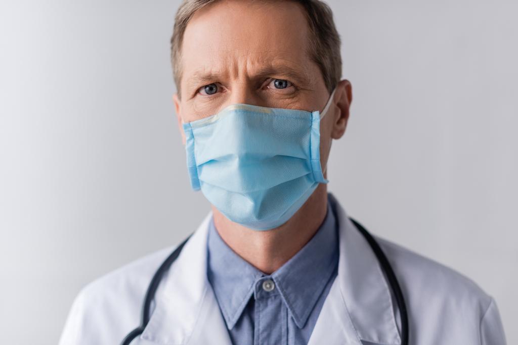 врач средних лет в синей медицинской маске на сером
  - Фото, изображение