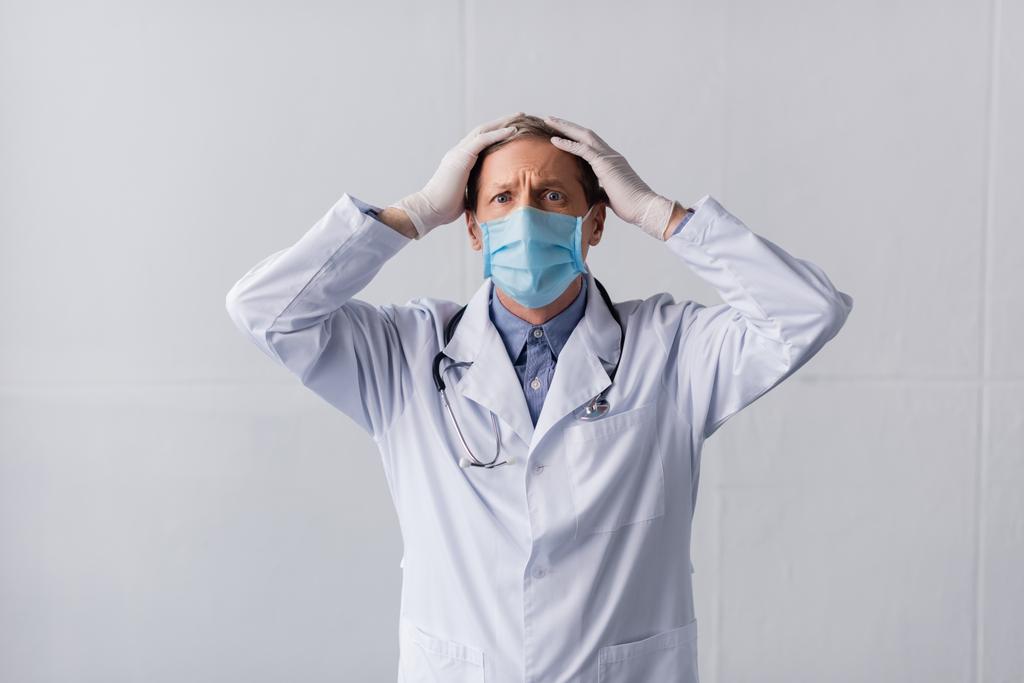 stressé médecin d'âge moyen en bleu masque médical touchant la tête sur gris
  - Photo, image