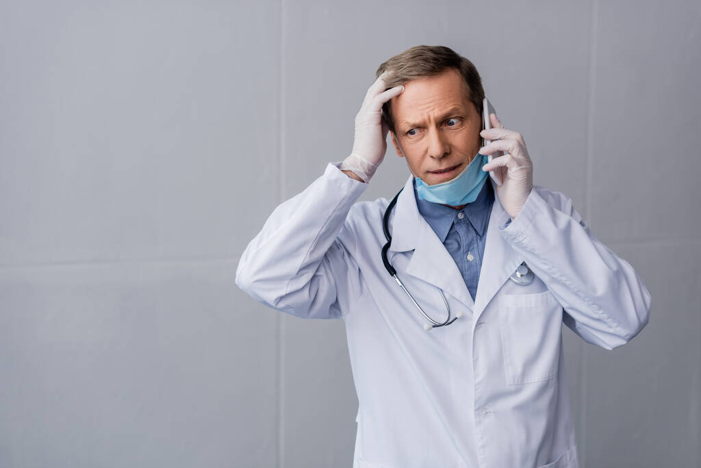 stressé médecin d'âge moyen parler sur smartphone et toucher les cheveux sur gris
  - Photo, image