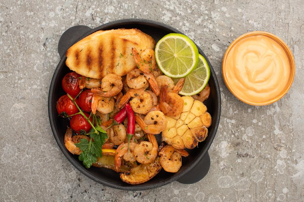 top view of fried shrimps with grilled toasts, vegetables and lime with sauce on grey concrete background - Photo, Image