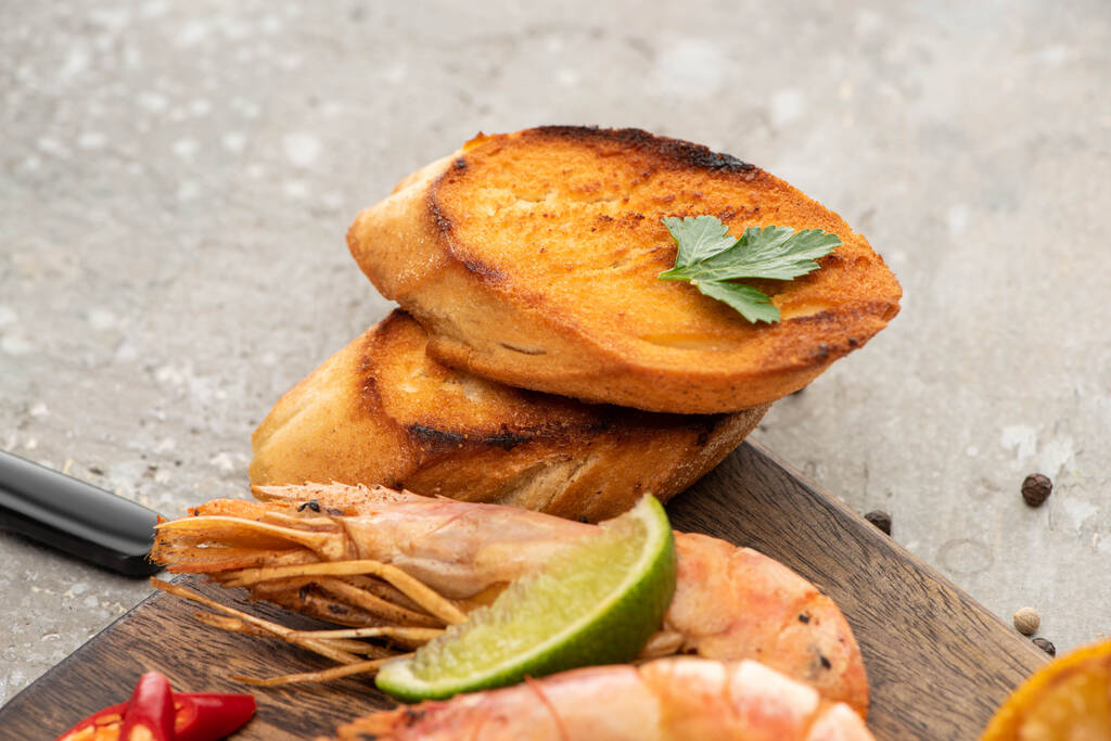 close up view of fried shrimps with grilled toasts and lime on wooden board on grey concrete background - Photo, Image