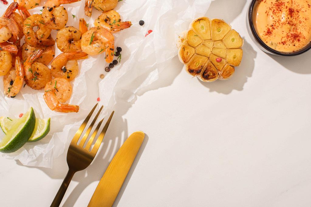 vista superior de camarones fritos sobre papel pergamino con cubiertos, maíz a la parrilla, pimienta, salsa y lima sobre fondo blanco
 - Foto, Imagen