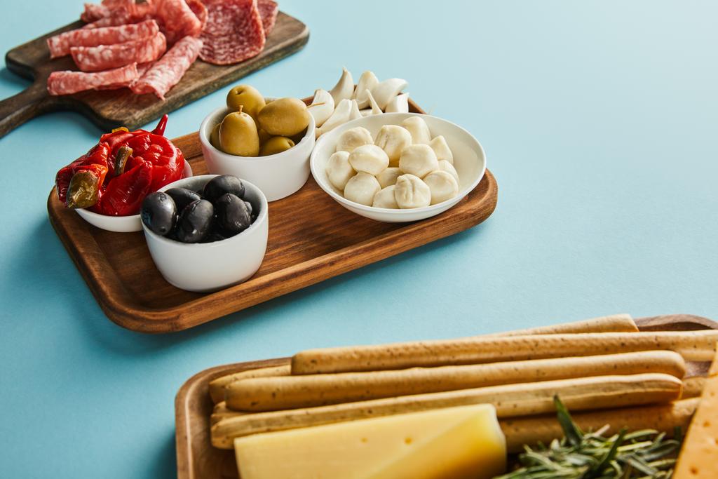 Hoge hoek uitzicht van antipasto ingrediënten op borden op blauw - Foto, afbeelding