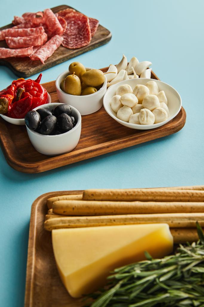 Hoge hoek uitzicht van antipasto ingrediënten op borden op blauwe achtergrond - Foto, afbeelding