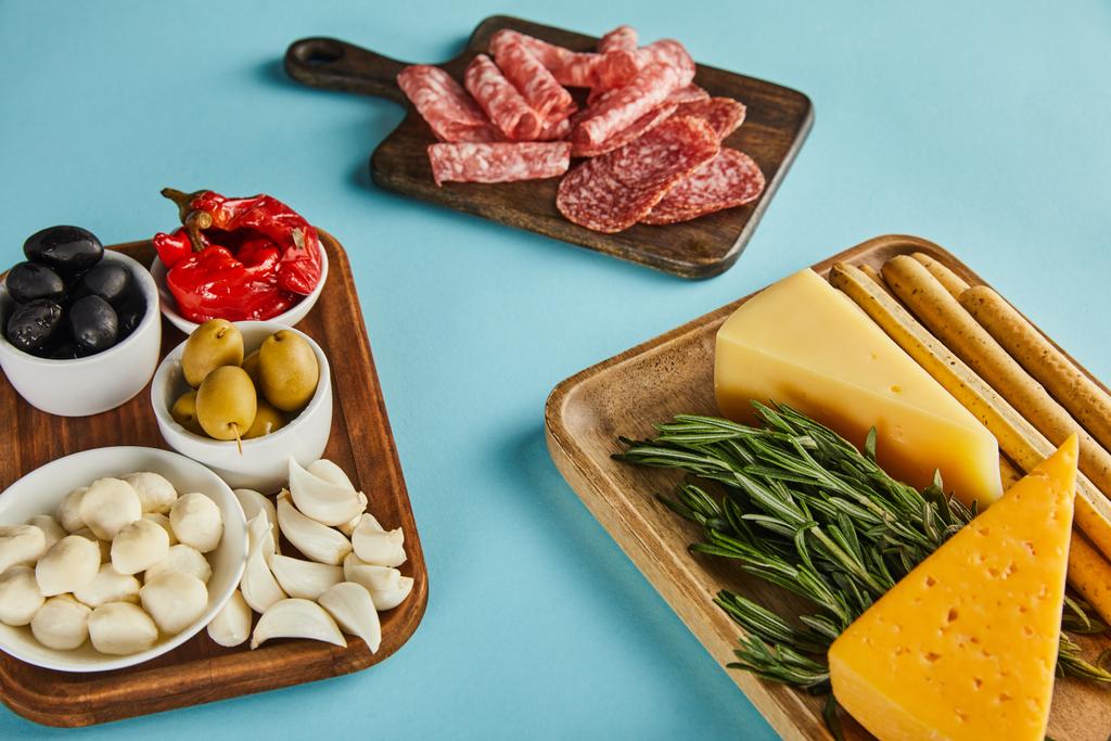 High angle view of salami slices and antipasto ingredients on boards on blue - Photo, Image