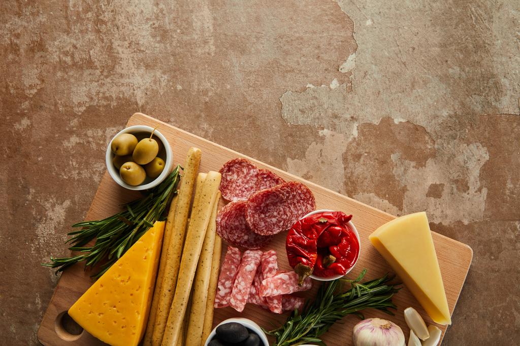 Horní pohled na tyčinky, sýr, plátky salámu a antipasto ingredience na palubě na hnědé - Fotografie, Obrázek