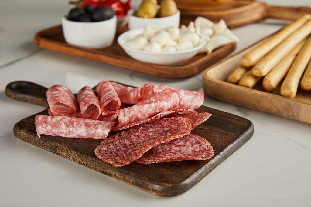 Selectieve focus van salami plakjes aan boord in de buurt van antipasto ingrediënten op wit - Foto, afbeelding