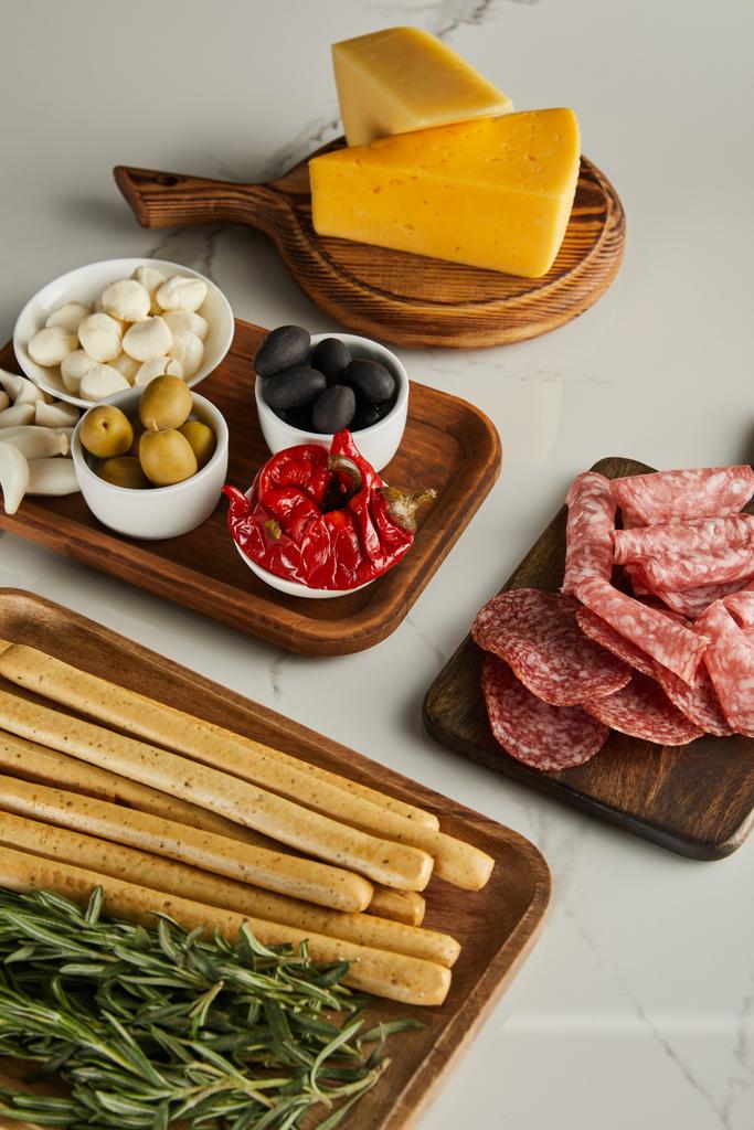 Vista en ángulo alto de tablas con palitos de pan, romero, rebanadas de salami, queso e ingredientes antipasto en blanco
 - Foto, Imagen