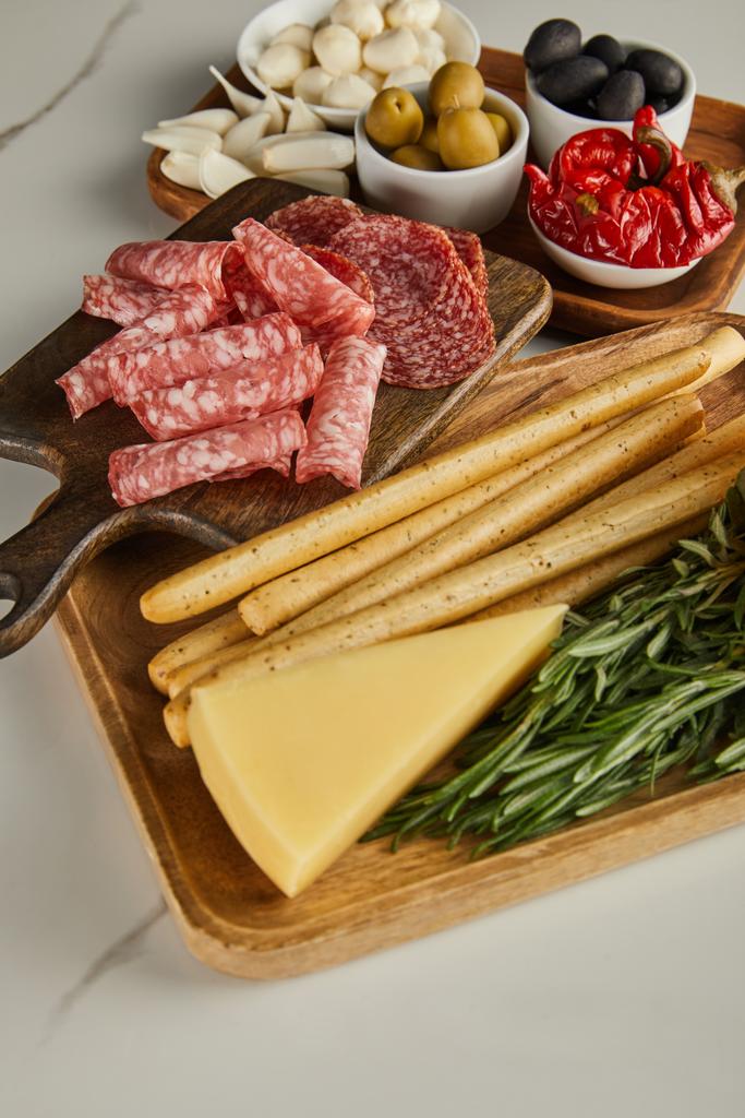 Vista en ángulo alto de tablas con rebanadas de salami, palitos de pan, queso e ingredientes antipasto sobre fondo blanco
 - Foto, Imagen