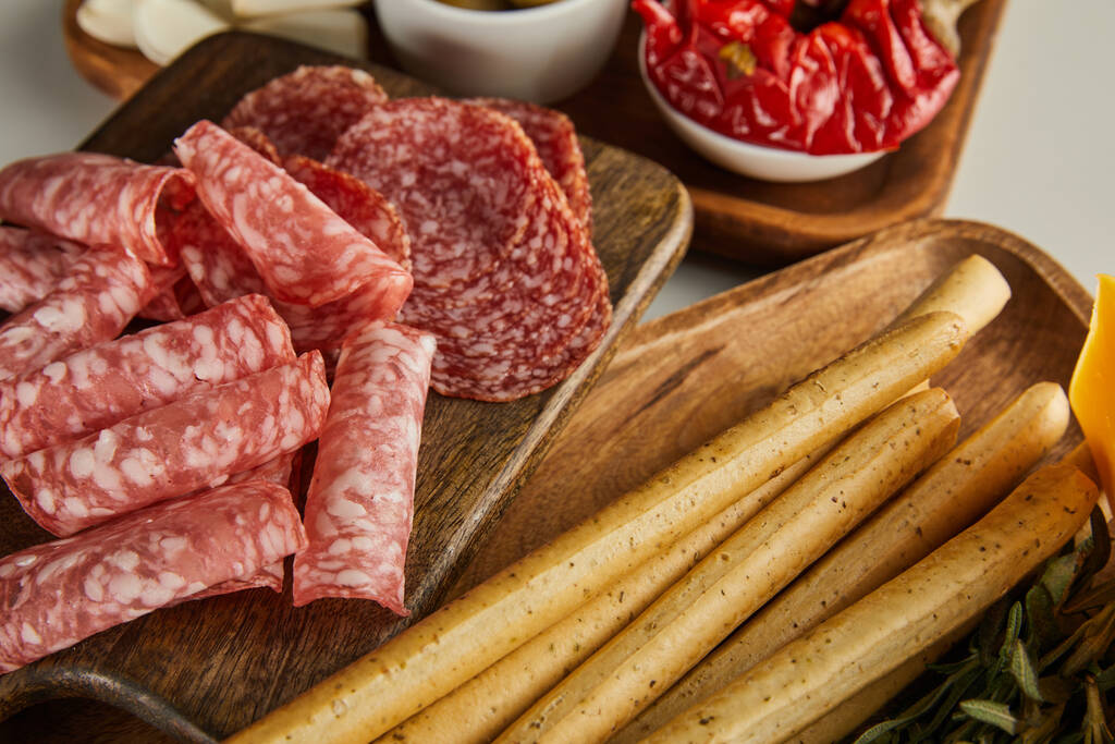 High angle view of salami slices, breadsticks and antipasto ingredients on boards on white background - Photo, Image