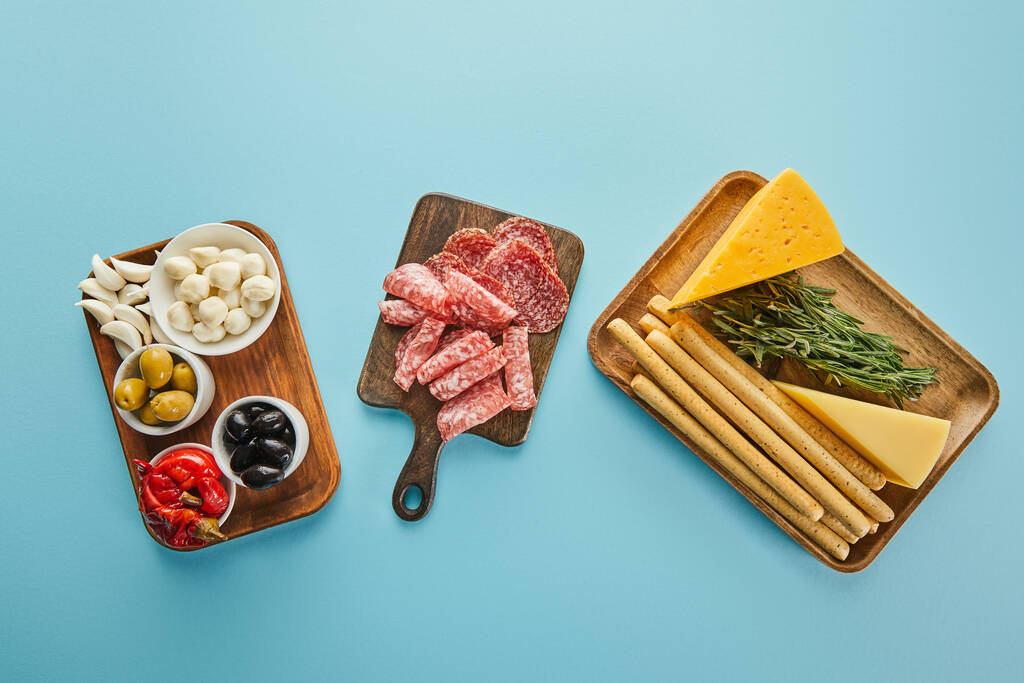 Bovenaanzicht van antipasto ingrediënten op borden op blauwe achtergrond - Foto, afbeelding