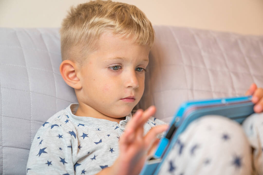 Ragazzo caucasico bambino utilizzando tablet digitale mentre sdraiato sul letto a casa
 - Foto, immagini