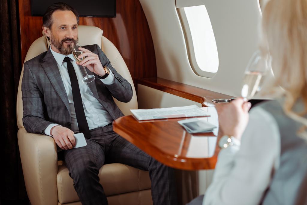 Selectieve focus van lachende zakenman met champagne op zakenvrouw in vliegtuig   - Foto, afbeelding