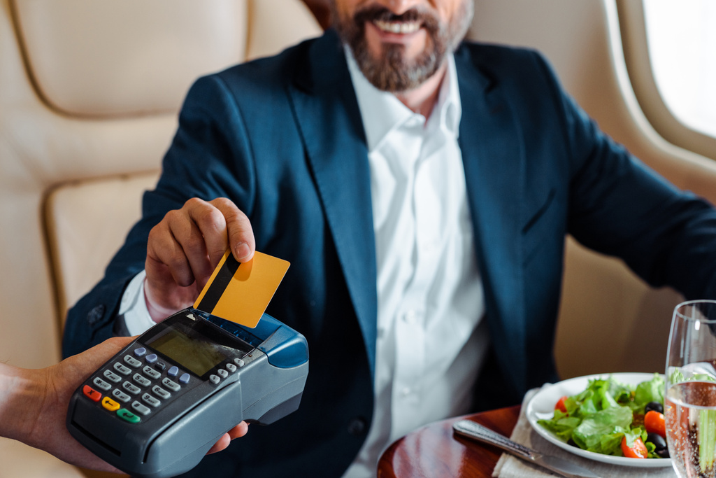 Enfoque selectivo de sonriente hombre de negocios pagando con tarjeta de crédito cerca de ensalada y copa de champán en avión
  - Foto, Imagen