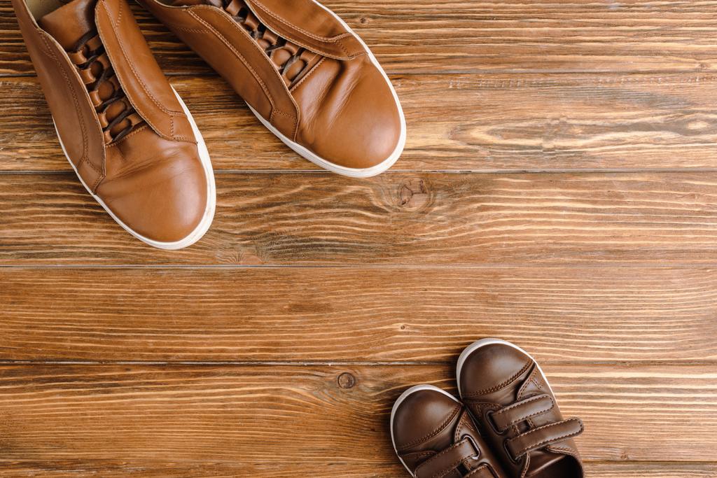 Вид зверху чоловічого та дитячого коричневого повсякденного взуття на дерев'яному фоні, концепція дня батьків
 - Фото, зображення