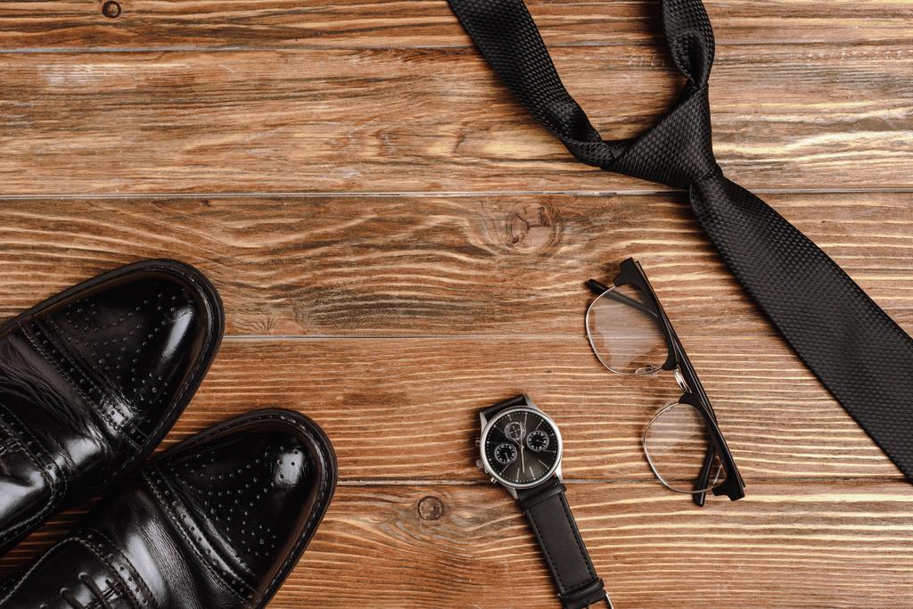 Flat lay com sapatos masculinos, gravata, relógio de pulso e óculos em fundo de madeira
 - Foto, Imagem