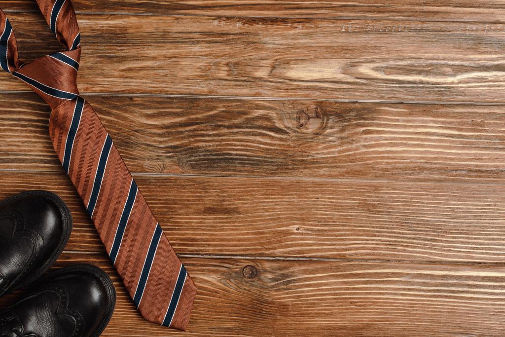 メンズシューズのトップビュー、木製の背景にエレガントなストライプのネクタイ - 写真・画像