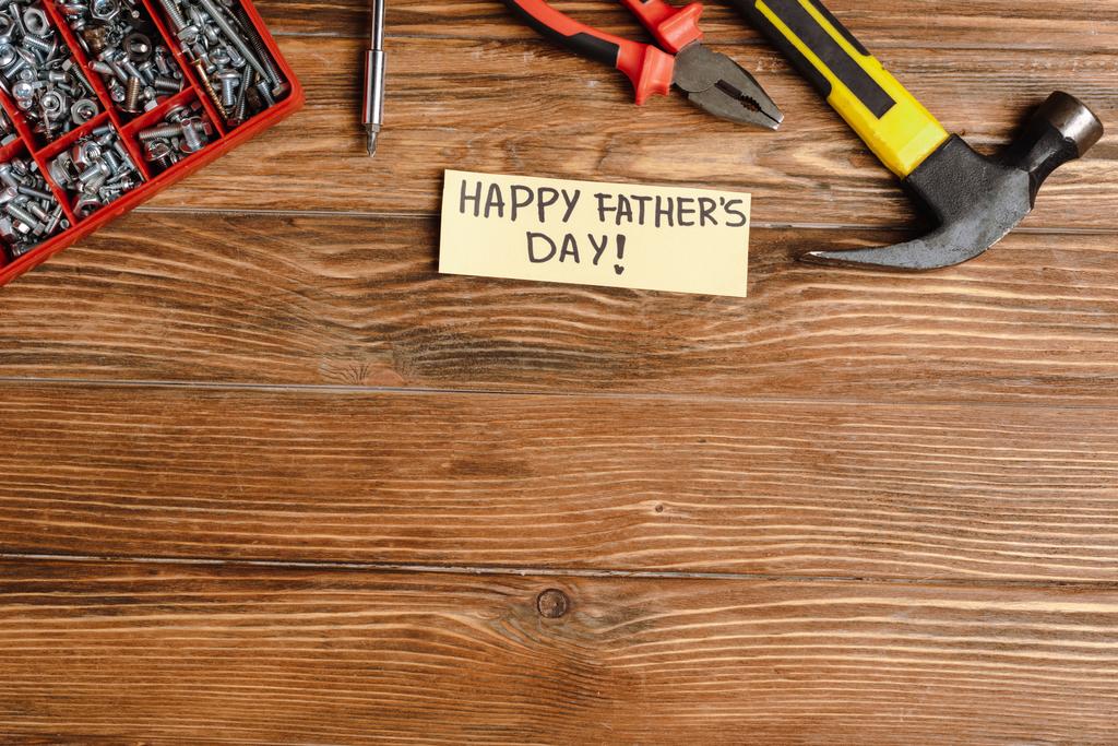 Widok z góry kartki z napisem pisanym ręcznie szczęśliwy dzień ojców, młotek, szczypce, śrubokręt, nakrętki i śruby na drewnianym tle - Zdjęcie, obraz